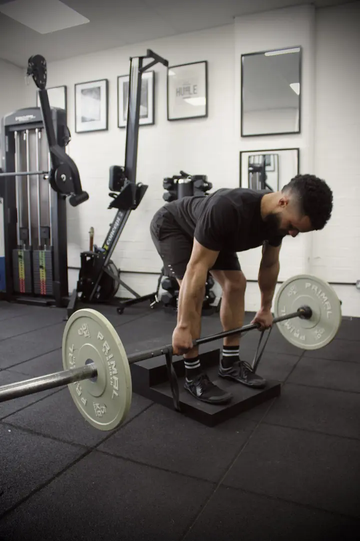 banded deadlift A man using the Forte Fitness step. He is stood on the lower step, and is bending over in a forward position while holding a bar with weights attached. His knees are bent to complete the deadlift maneuver.