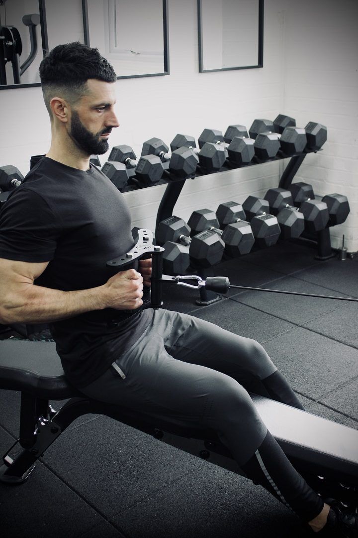 cable row movement finish A man using the Forte Fitness cable row attachment. The man is sat on a gym bench, with the attachment pulled below at his chest with his elbows in line with his body.